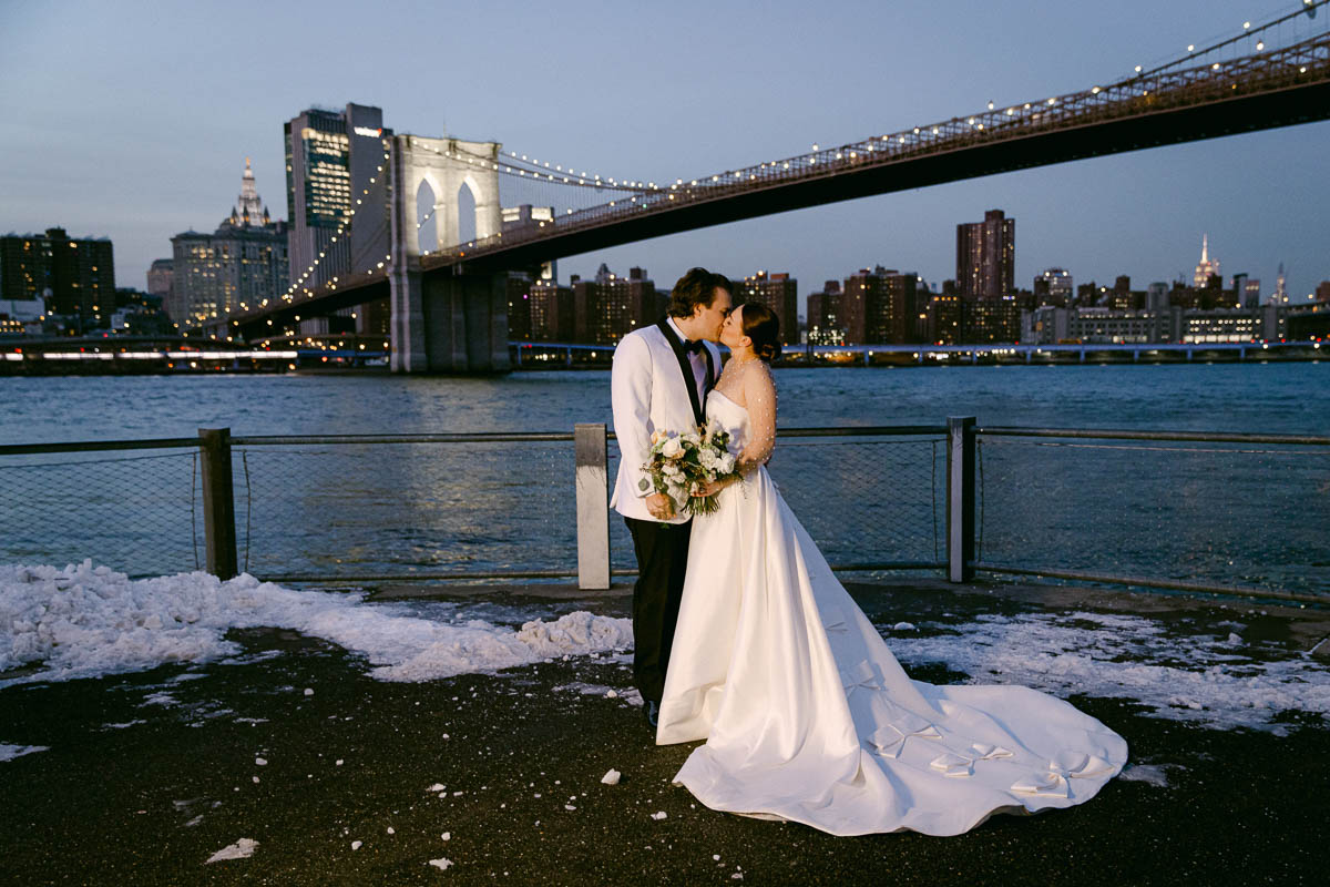 A bride and groom kiss at twilight at the Brooklyn Bridge
